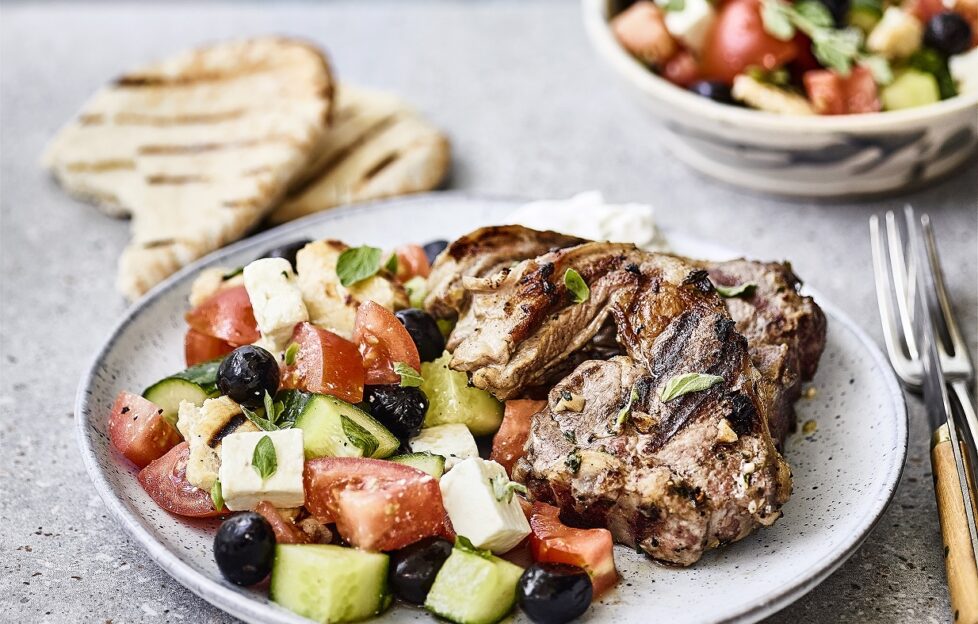 Greek feta and oliva salad with lamb chops on a plate and bread accompaniment