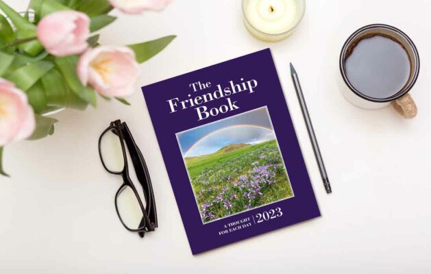 The Friendship Book on desk with flowers, glasses, pencil, candle and cup of tea