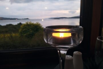 View of the sea out the window with a glass and candle in foreground