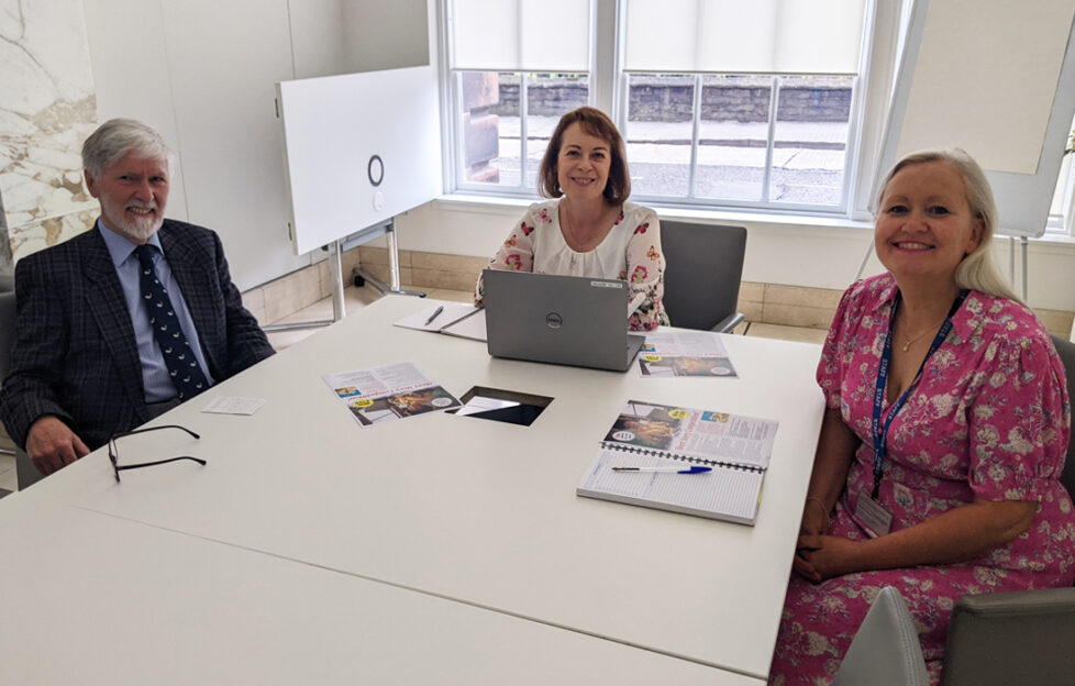 Robin, Angela and Lucy sitting around a desk smiling at the camera