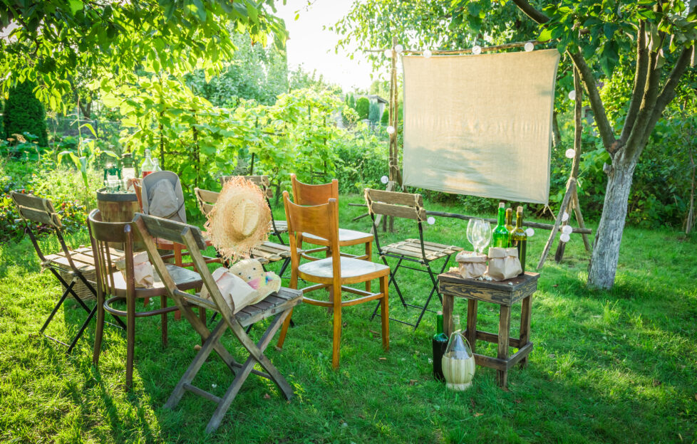 Garden cinema, white sheet screen with assorted wooden chairs
