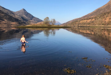 Woman wading into loch waters for wild swimming