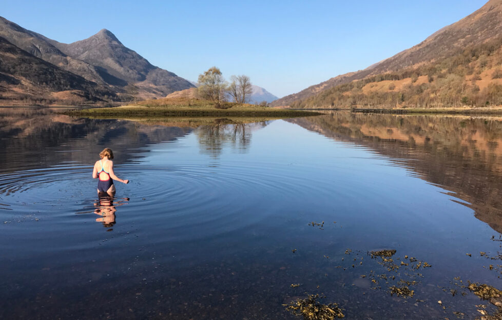 Woman wading into loch waters for wild swimming