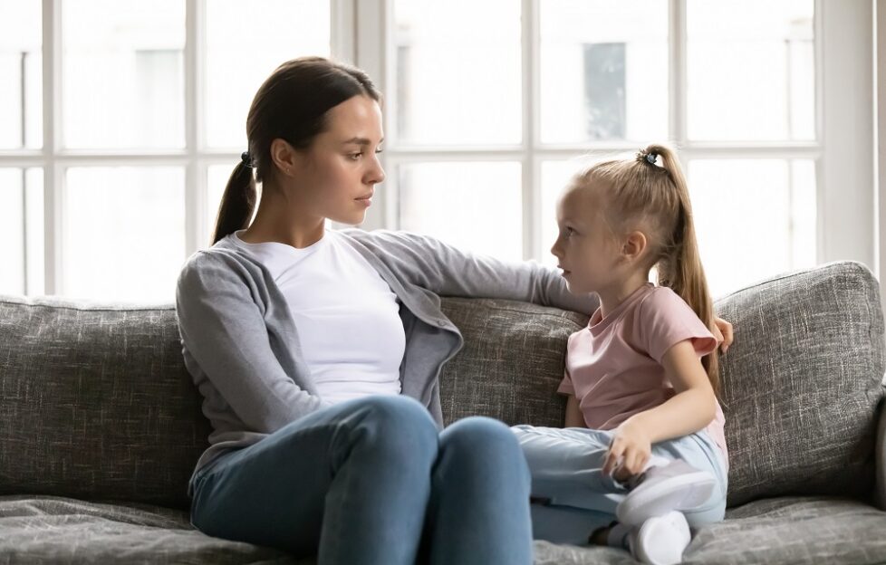 Mother talking seriously with a child on grey sofa