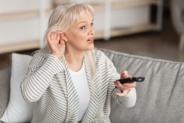 Middle-aged woman holding hand to ear struggling to hear the TV