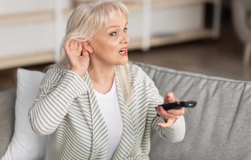 Middle-aged woman holding hand to ear struggling to hear the TV