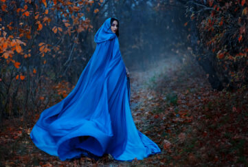 historical woman wearing blue cloak walks into mysterious wood