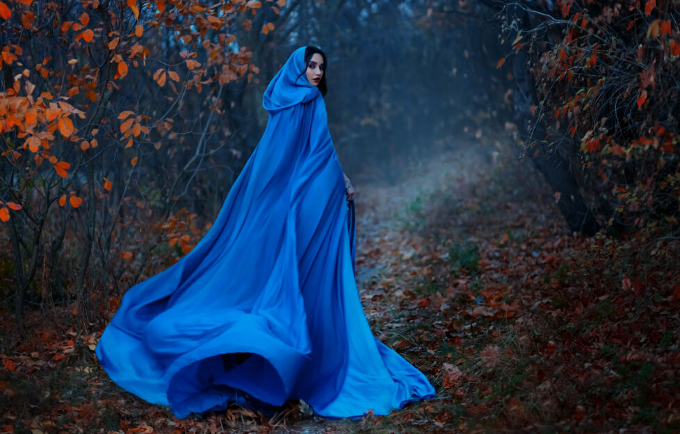 historical woman wearing blue cloak walks into mysterious wood