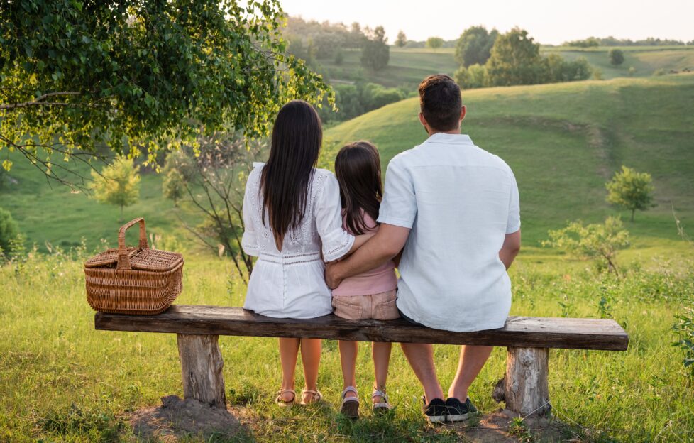 Man and woman with young child sitting on a park bench looking out at green landscape view from behind