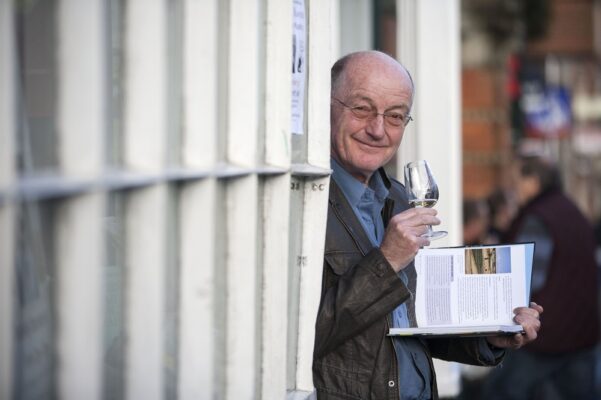 Oz Clarke smiling from a doorway holding a book