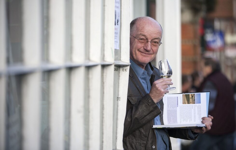 Oz Clarke smiling from a doorway holding a book