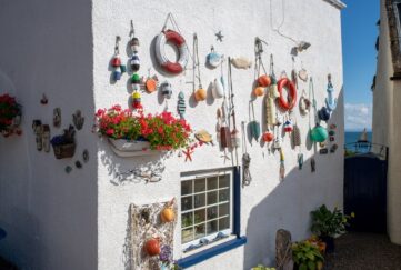 A white wall side of a house covered in hanging decorations and colourful flowers