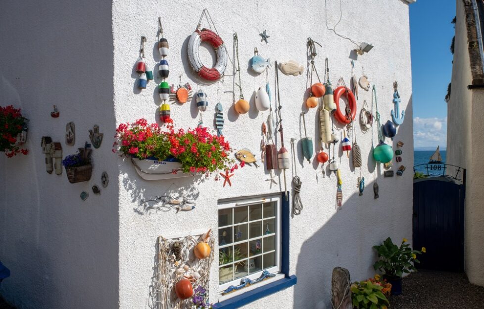 A white wall side of a house covered in hanging decorations and colourful flowers