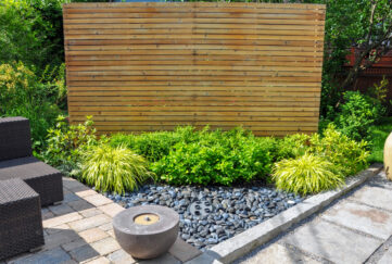 A garden corner with wood feature, shrubs, square paving, round stone feature and square seating