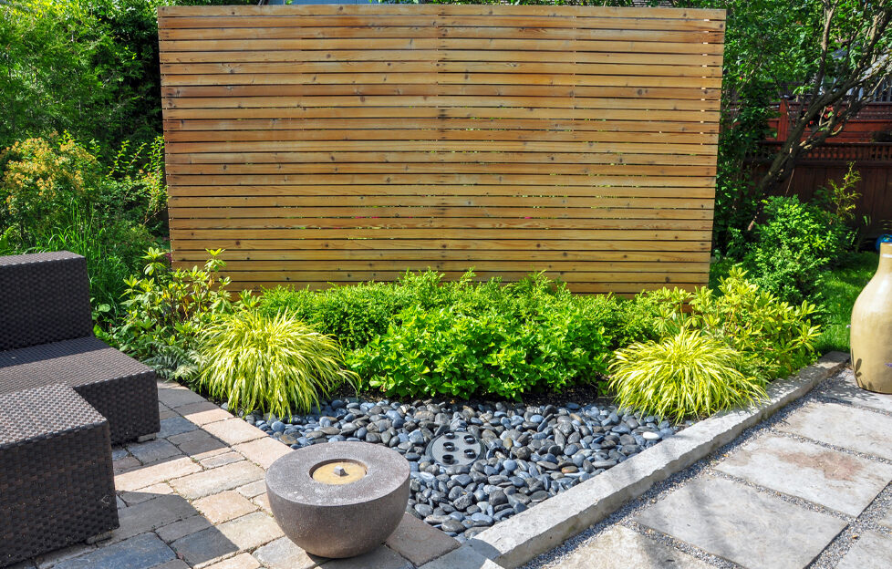 A garden corner with wood feature, shrubs, square paving, round stone feature and square seating