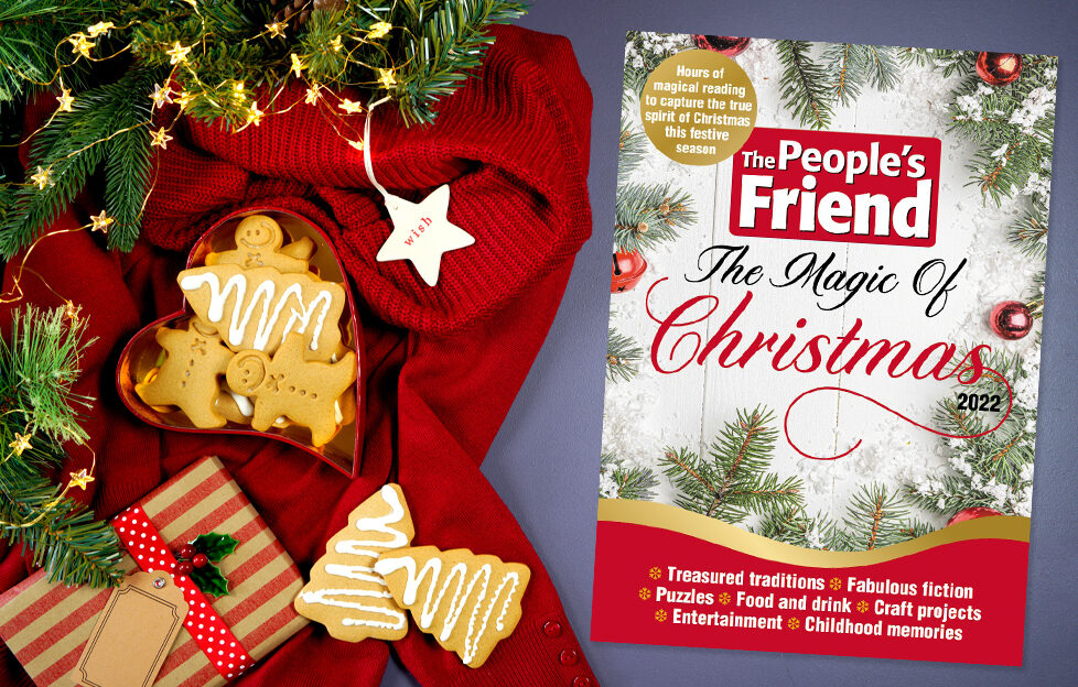 Cover Of The People's Friend Magic Of Christmas bookazine on Christmas flatlay with red blanket, biscuits and present
