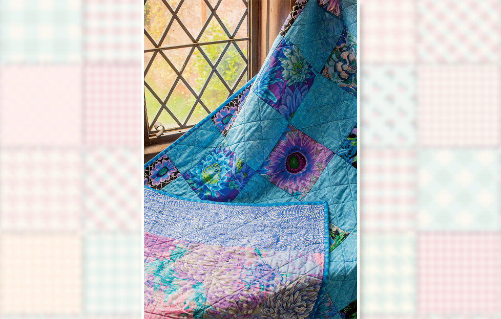 Blue Kaffe Fassett patchwork quilt being held up next to a window