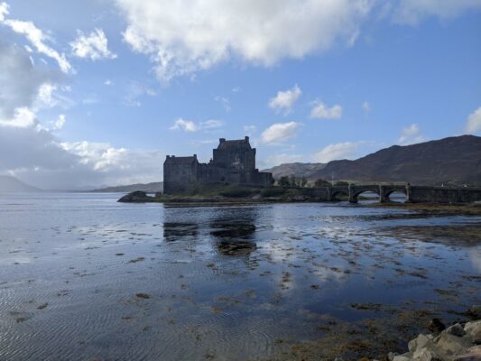 Eilean Donan castle and its bridge above the loch and against hills in the back on a blue sky day