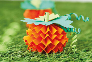 Orange papercraft pumpkins from zig zag paper, green leaves on grassy background