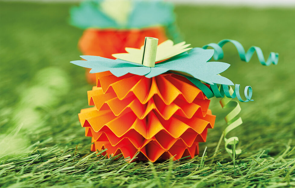 Orange papercraft pumpkins from zig zag paper, green leaves on grassy background