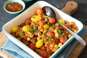 A roasting dish filled with veg to make a vegan curry, tomatoes and chickpeas