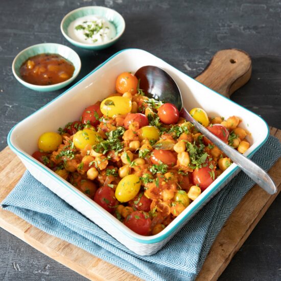 A roasting dish filled with veg to make a vegan curry, tomatoes and chickpeas