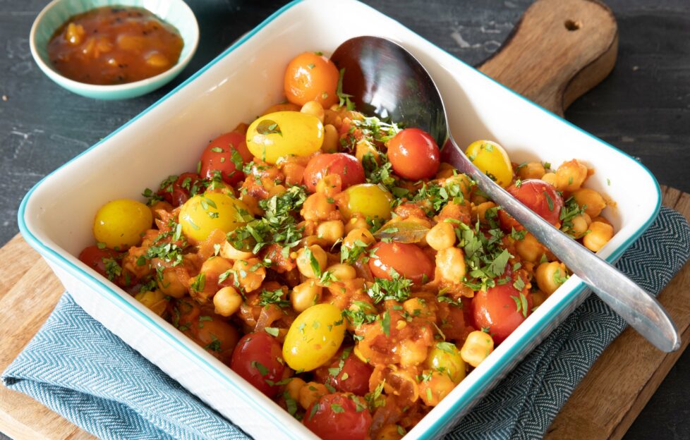 A roasting dish filled with veg to make a vegan curry, tomatoes and chickpeas