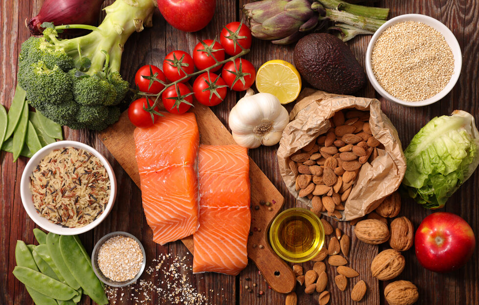 A flatlay of healthy foods such as salmon, tomatoes, seeds, nuts, broccoli