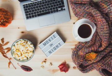 Flatlay of laptop, coffee, blankey, popcorn and a light box sign saying Movie Night