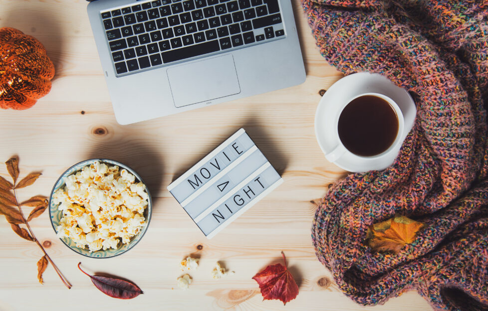 Flatlay of laptop, coffee, blankey, popcorn and a light box sign saying Movie Night