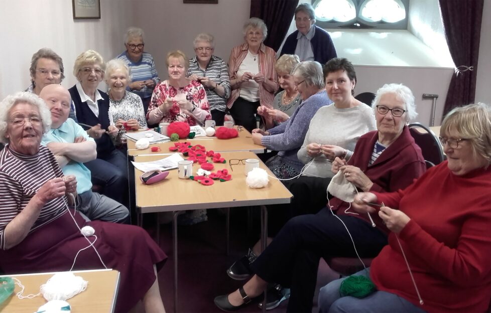 A group of crafters gathered around a table of wool and knitted or crocheted poppies