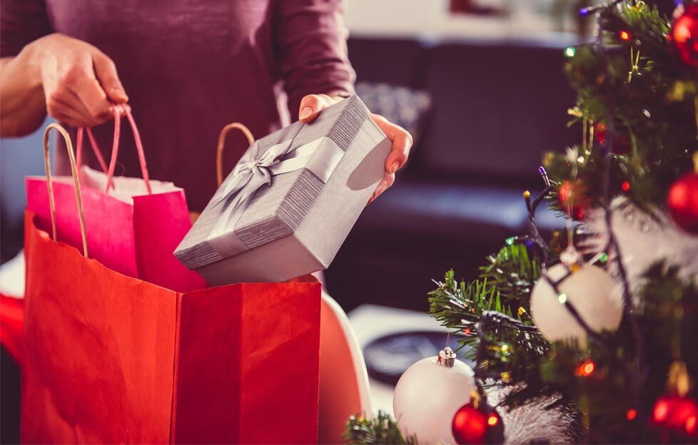 Woman putting Christmas presents in a gift bag next to a tree