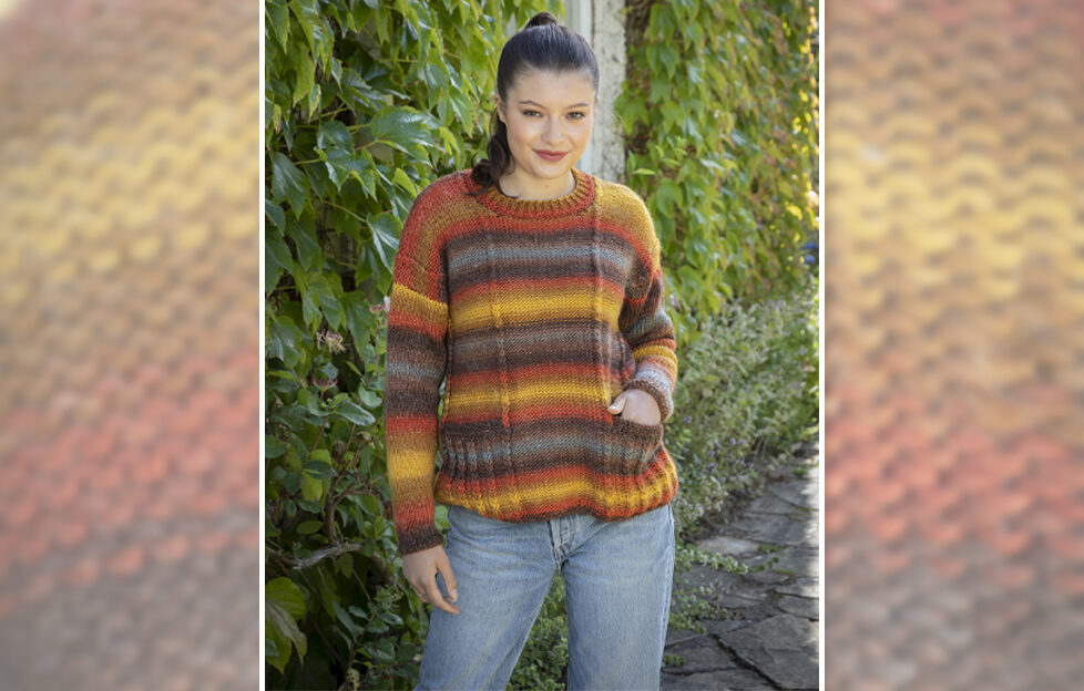 Model wearing easy knit sweater with blue jeans and brown hair in front of hedge