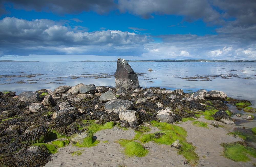 A solo standing stone on a rocky beach looking out to the water and horizon