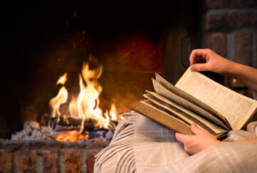 Hands holding a book on a blanket in front of a wood fire