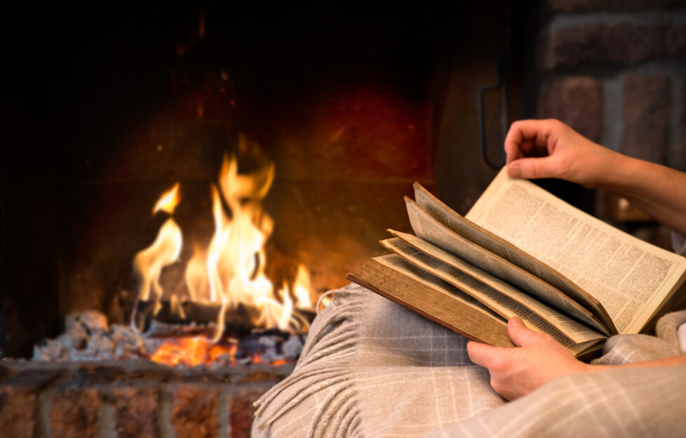 Hands holding a book on a blanket in front of a wood fire