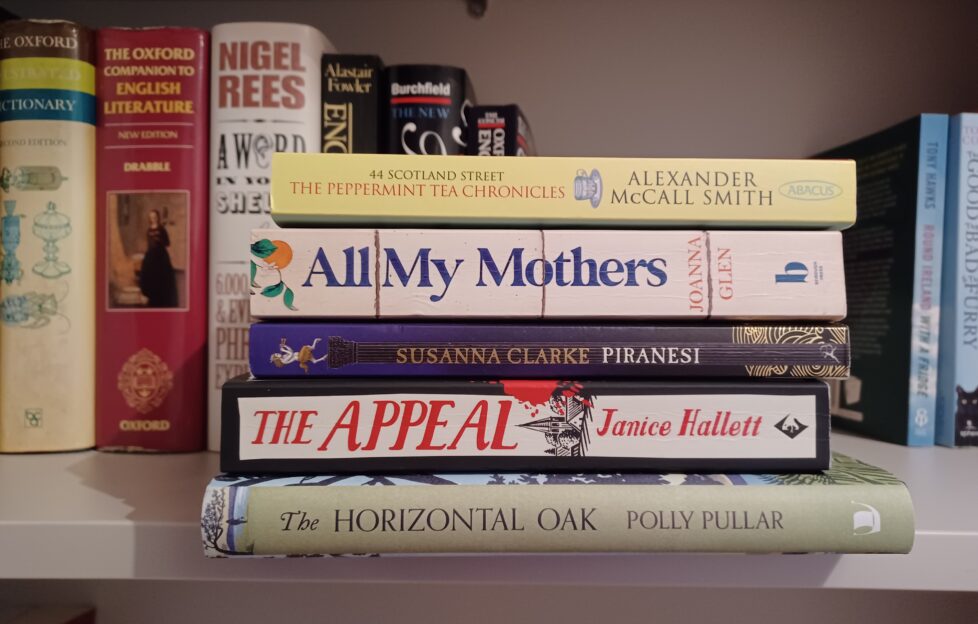 A stack of books on Angela's bookshelf showing spines of The Horizontal Oak, The Appeal, Piranesi, All My Mothers and The Peppermint Tea Chronicles