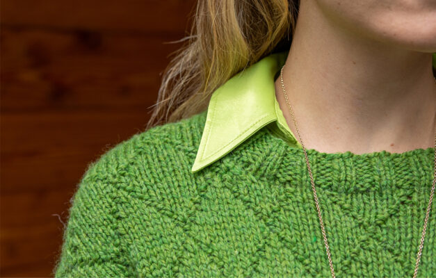 Close up of woman's shoulder and neck with detail of green diamond knitted sweater and a lighter green shirt collar underneath
