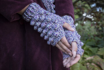 Lilac crochet gloves on model's hands wearing dark purpler coat