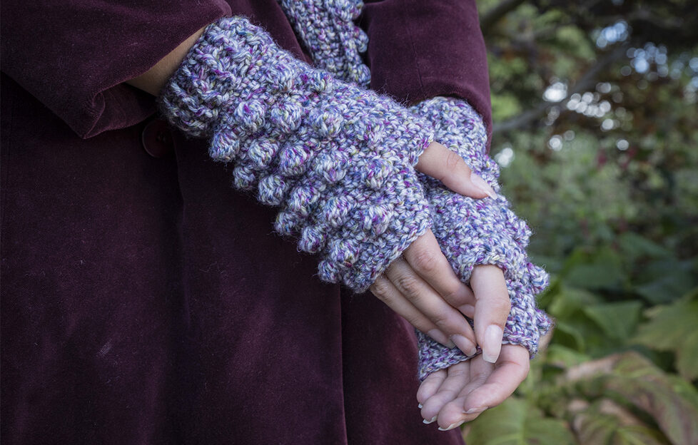 Lilac crochet gloves on model's hands wearing dark purpler coat