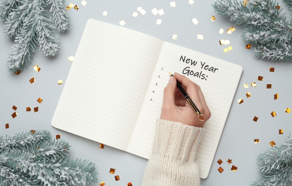 person writing new year goals in a notebook on festive flatlay