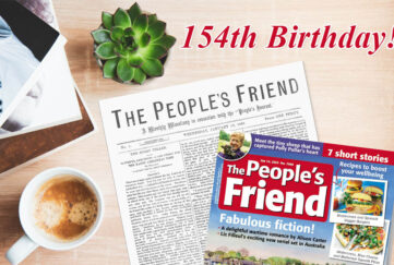 A flatlay of the original first issue of The People's Friend with the current issue on top, next to a coffee, pile of books and succulent