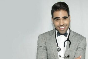 Dr Ranj Singh in a grey jacket with stethoscope smiling at the camera on a plain grey background