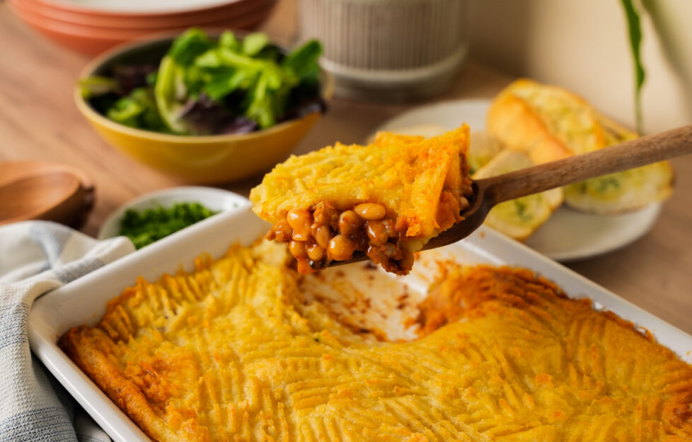 A spoonful of Heinz Beans Spiced Bean pie made from mashed potatoes over the top of the casserole dish of pie on a kitchen counter top