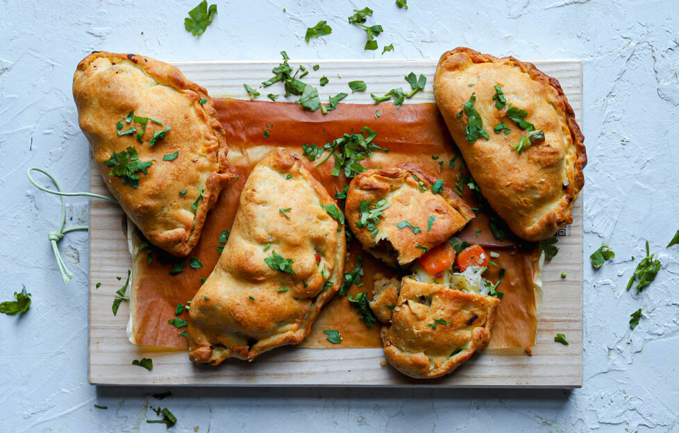 Flatlay of Welsh Oggie (pasty) recipe on chopping board, one cut with vegetable filling revealed