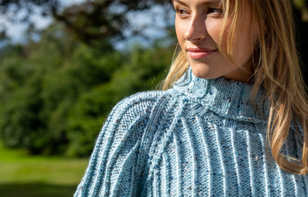 Close up of woman's face looking sideways and the neck/shoulder of the knitted cosy ribbed sweater in light blue