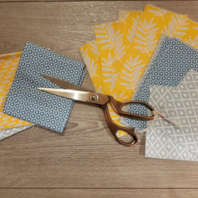 Flatlay of grey and mustard patterned fabric squares and craft scissors