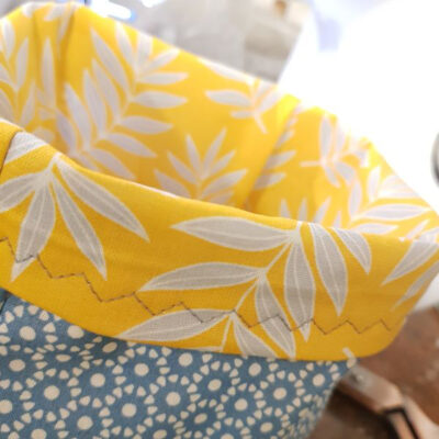 Close up of top of mustard and grey fabric storage box, mustard with grey leaf patterns and close up of stitching