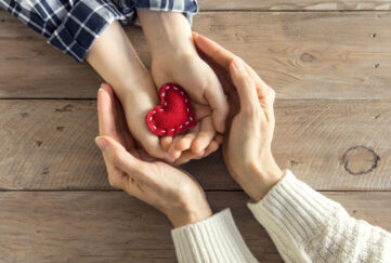 Young hands holding felt stitched heart and older hands cupping around them
