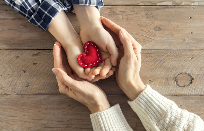 Young hands holding felt stitched heart and older hands cupping around them